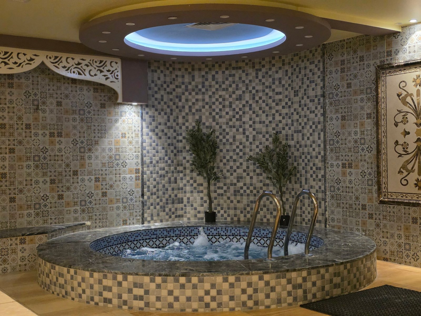 A serene indoor spa setting featuring a mosaic tiled jacuzzi with ambient lighting.