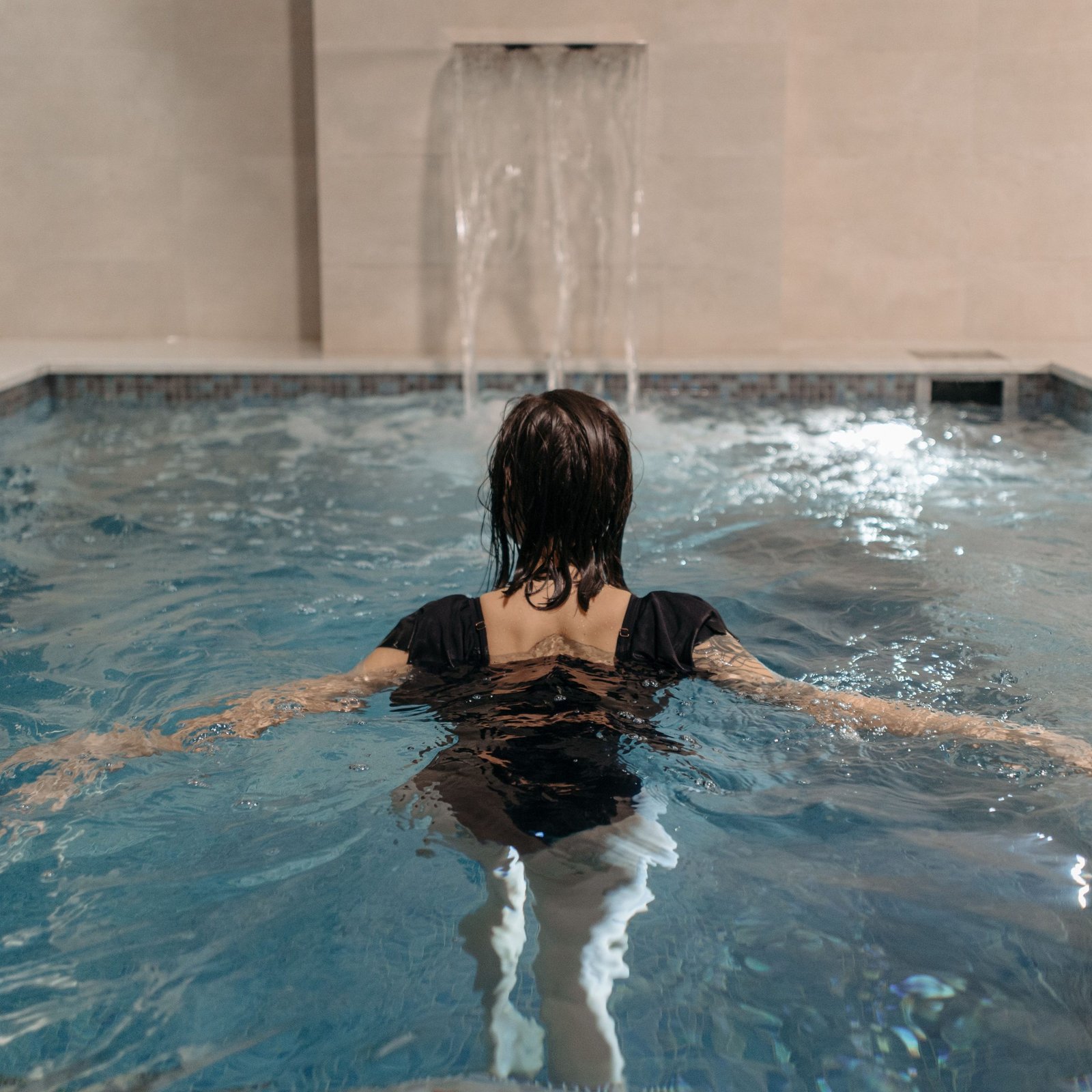 A woman enjoying a swim in an indoor pool with a waterfall feature.