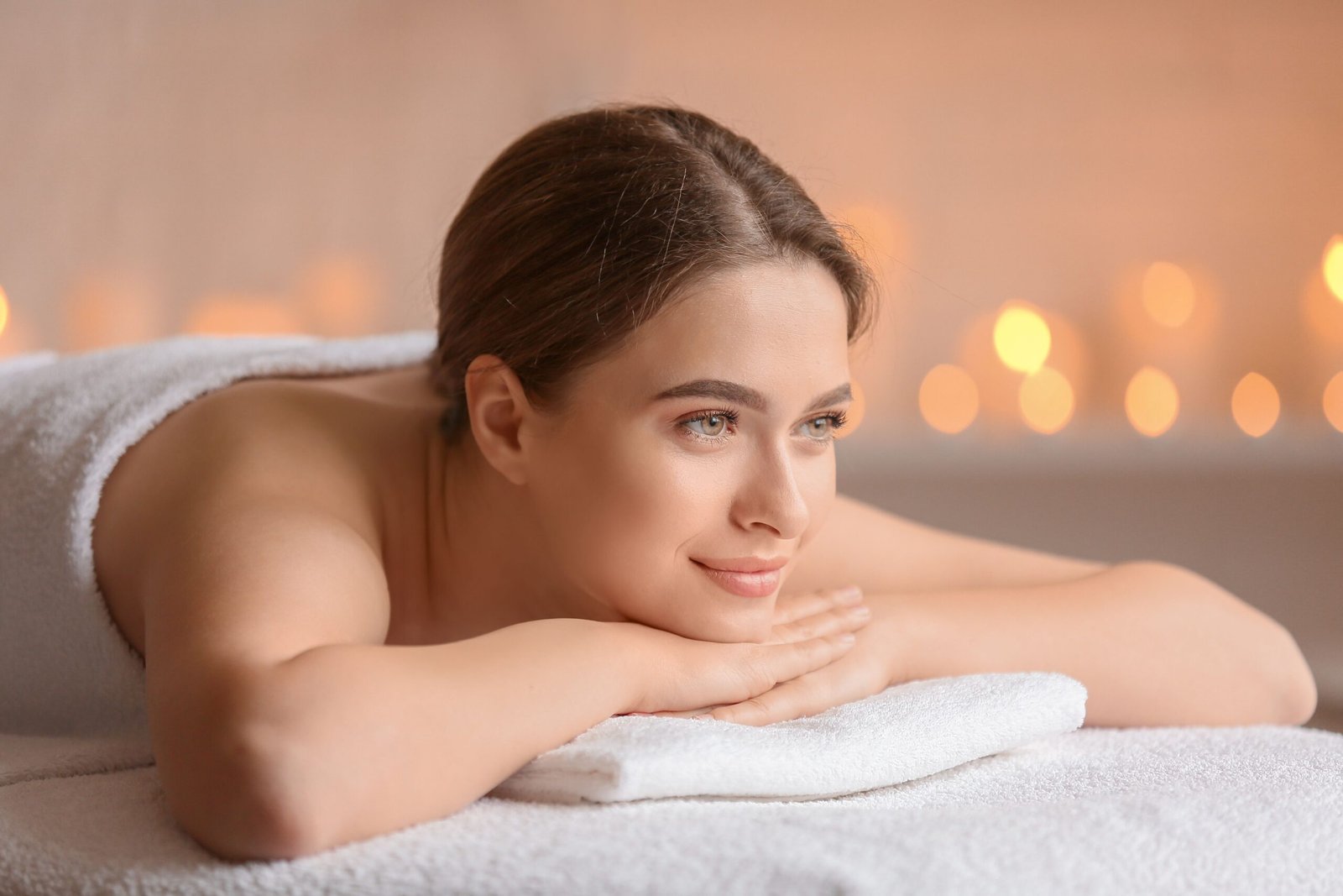 A serene woman enjoying a spa experience with flickering candles, wrapped in a towel, portraying pure relaxation.